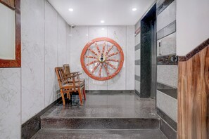 A marble wall with a large decorative wheel, a wooden chair, and a staircase leading to a higher floor. - Super Townhouse Oak Dharwad New Bus (Dharwad)