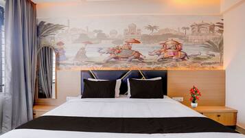 Een hotelkamer met een grote muurschildering van een traditioneel tafereel, een bed met zwart-wit beddengoed en een nachtkastje met een bloevas.