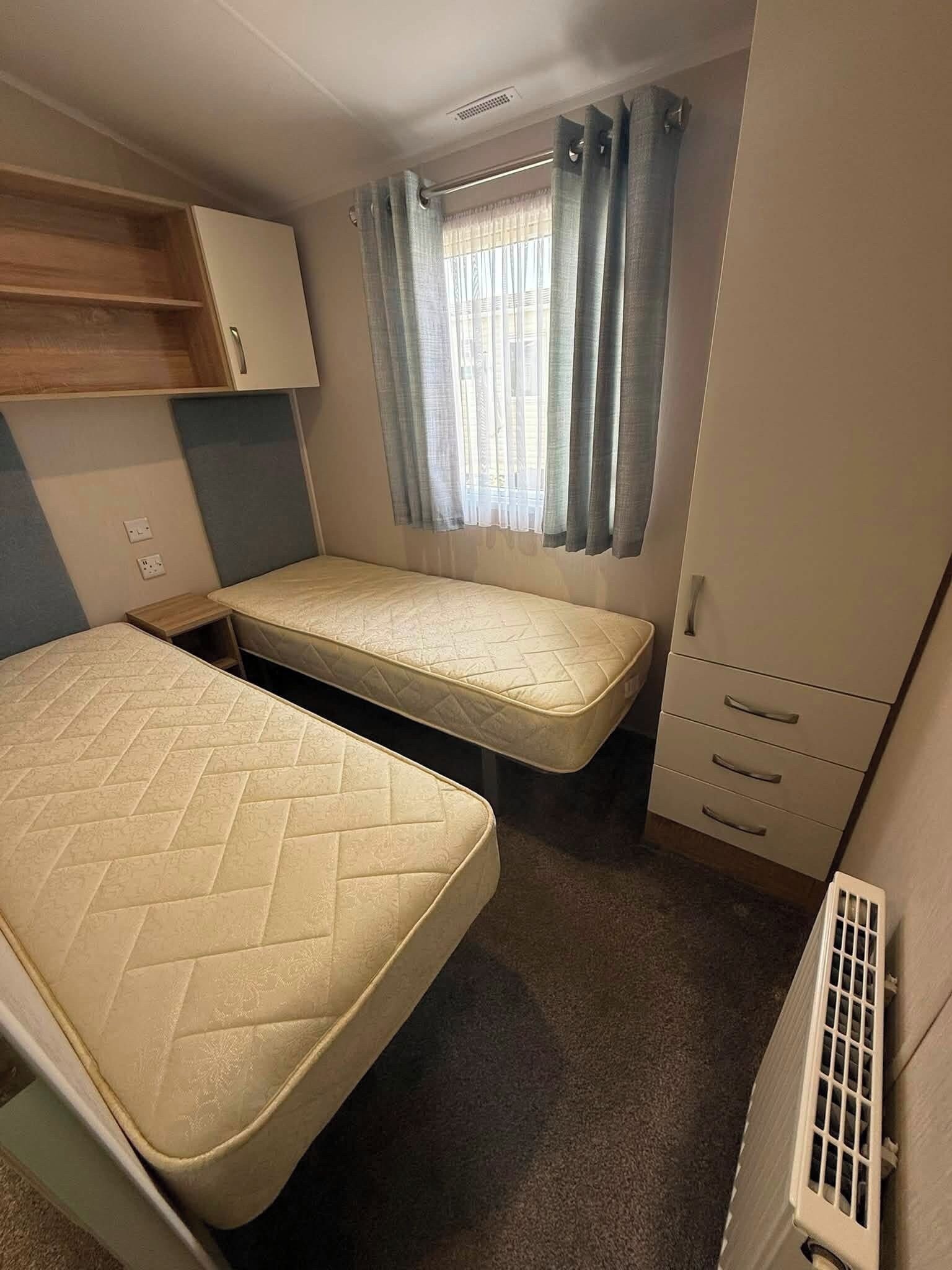 Une pièce de taille modeste comprenant un lit, un petit bureau, une armoire et une fenêtre avec des rideaux.