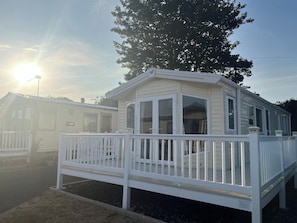 A mobile home with a fenced deck, large windows, and a clear sky. - Home by the Sea - Adventure Village Access (Great Yarmouth)