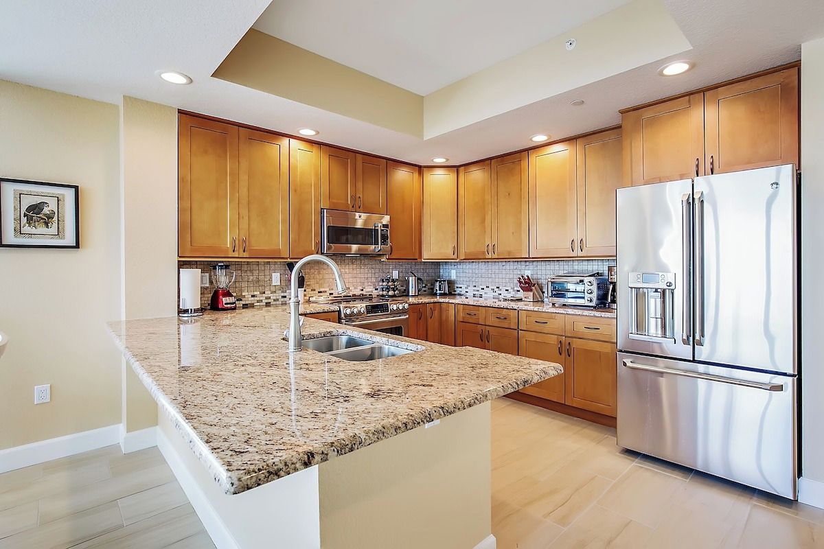A modern kitchen with granite countertops, stainless steel appliances, wooden cabinets, and a central island.