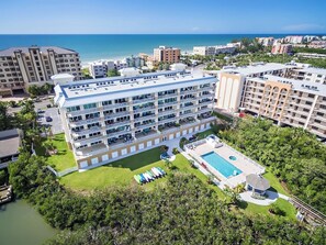 A multi-story hotel with a pool, surrounded by greenery and a view of the ocean. - Sunny 3-bedroom condo with views in peaceful Indian Shores (Indian Shores)