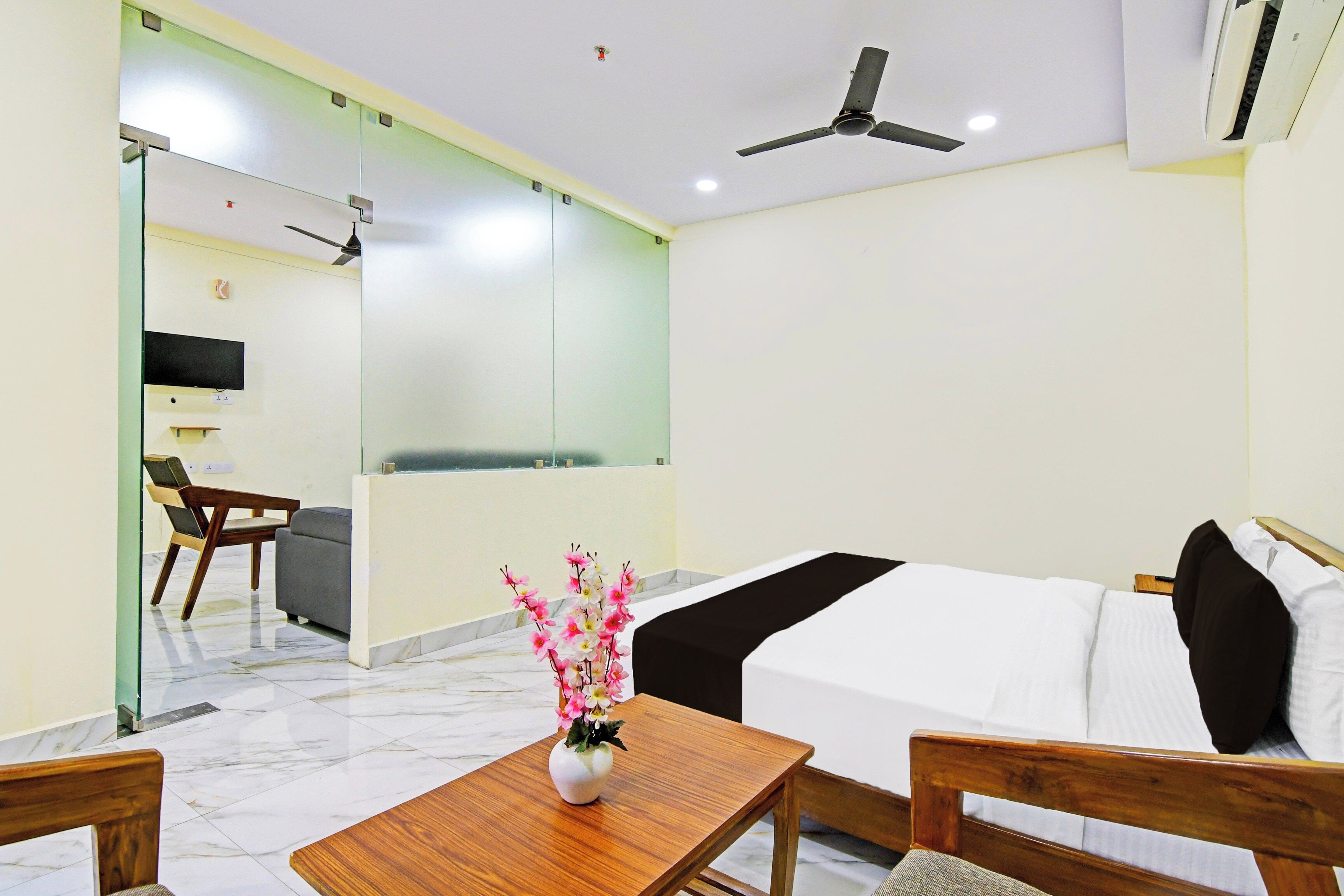 A hotel room with a bed, a desk, a chair, a vase with flowers, a ceiling fan, and a television.