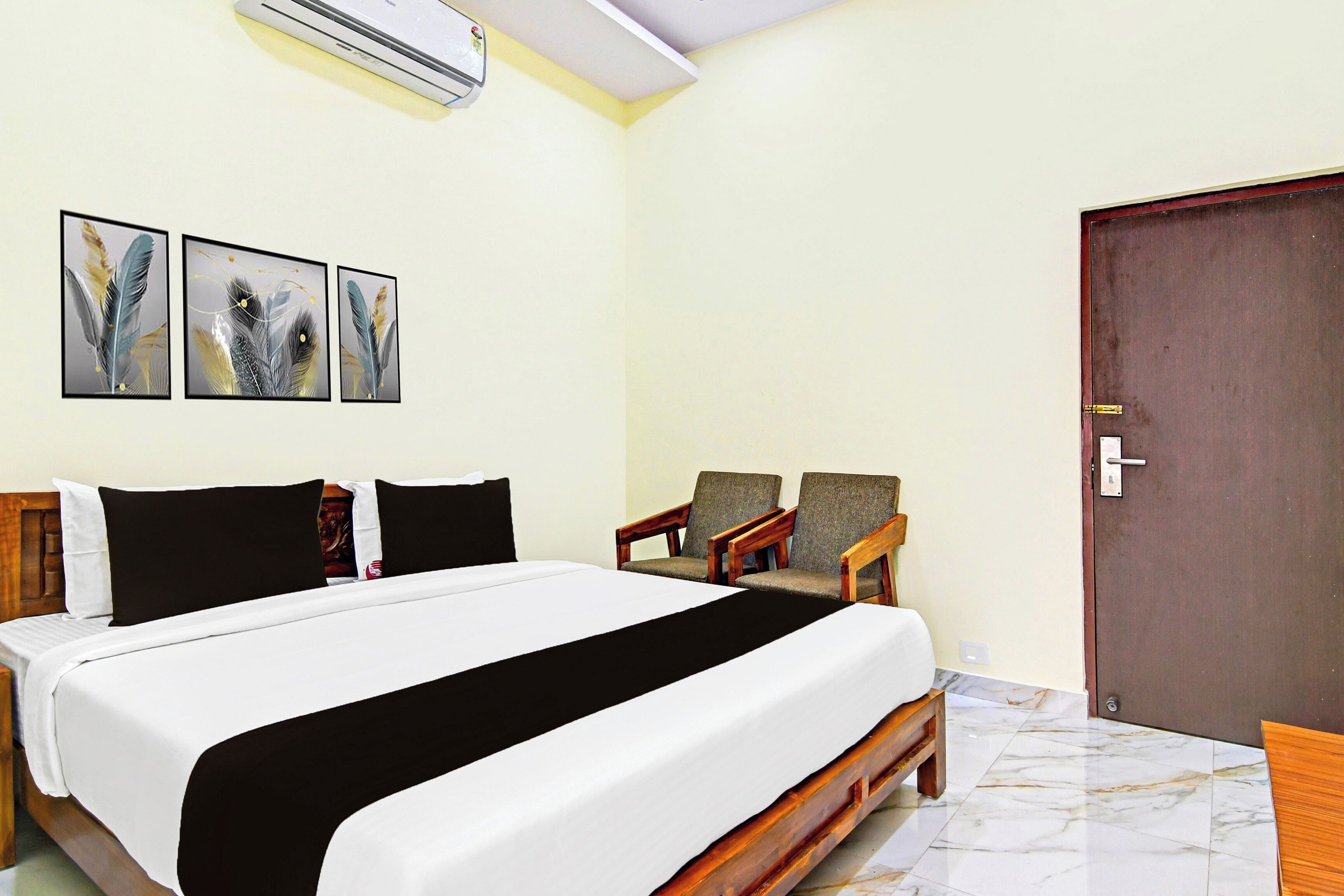A hotel room with a bed, two chairs, a door, and three feather wall art pieces.