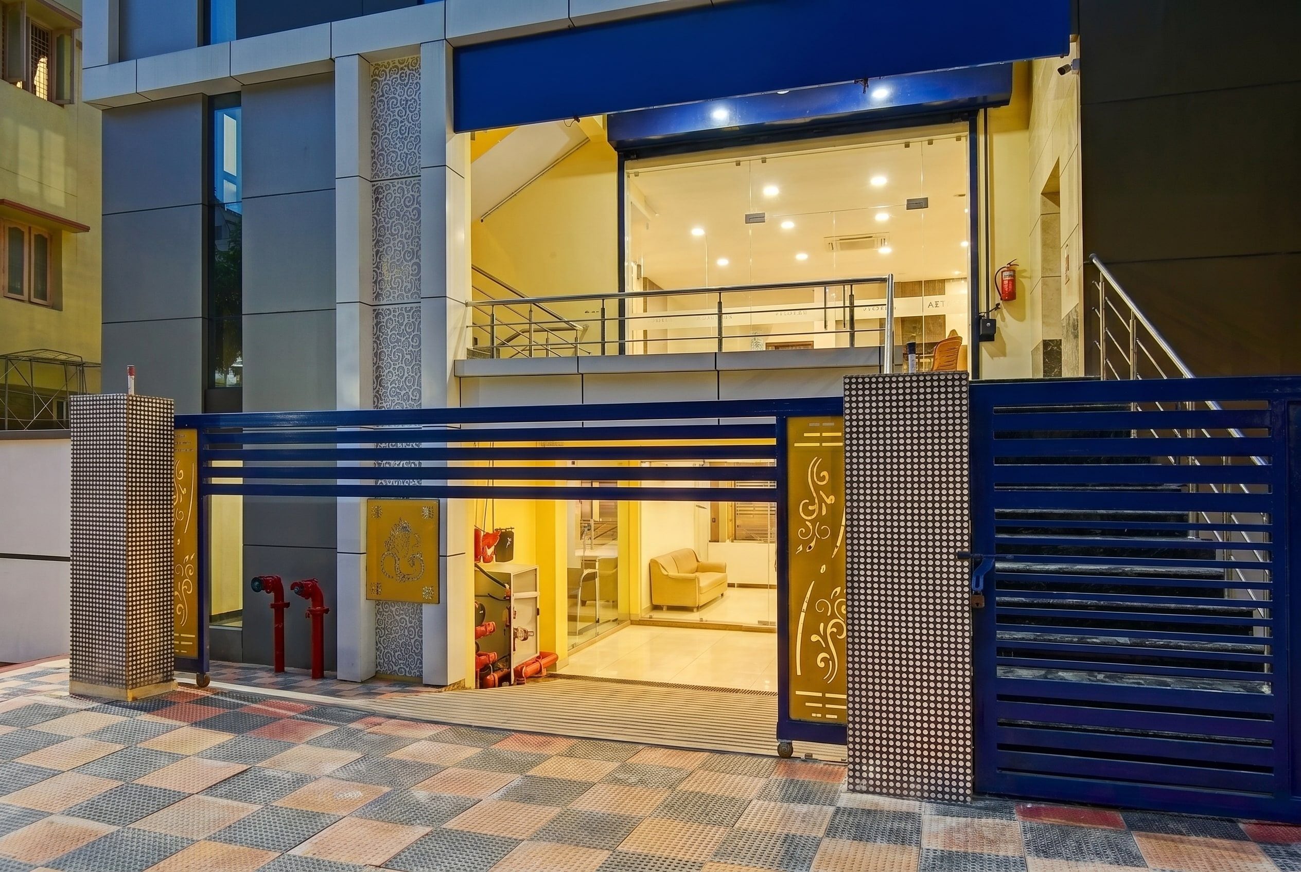 Entrada de hotel con una verja azul, una rampa accesible para sillas de ruedas y un extintor visible.