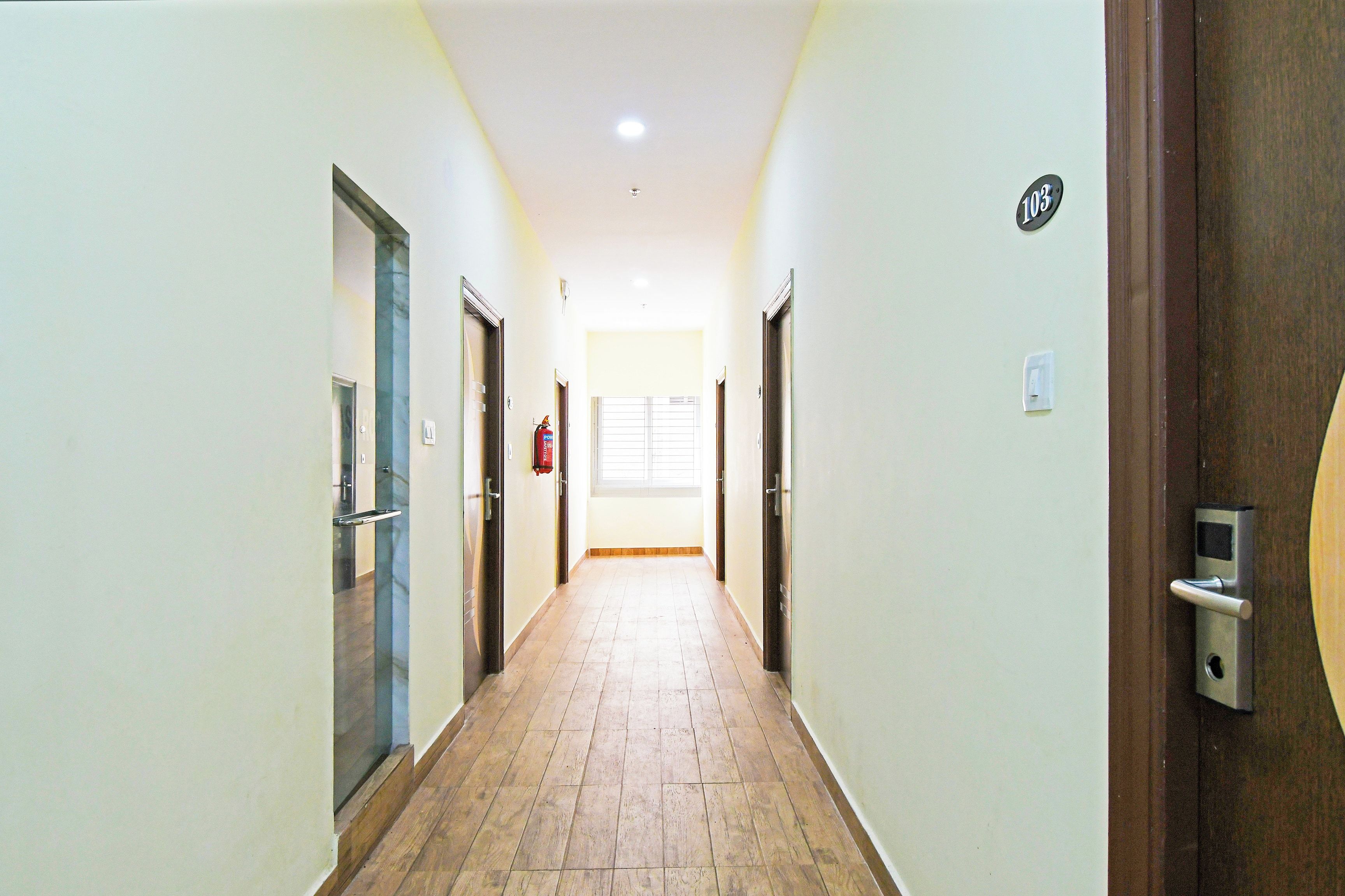 A corridor with doors on both sides, a fire extinguisher, and a window at the end.