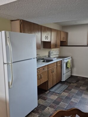 A kitchen with a white refrigerator, wooden cabinets, a sink, and a stove.