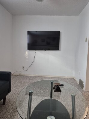 Une pièce dotée d’un téléviseur à écran plat fixé au mur, d’une table basse en verre et d’un canapé noir.