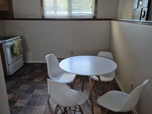 Una cocina compacta con una mesa redonda y cuatro sillas, estufa y ventana con persianas.