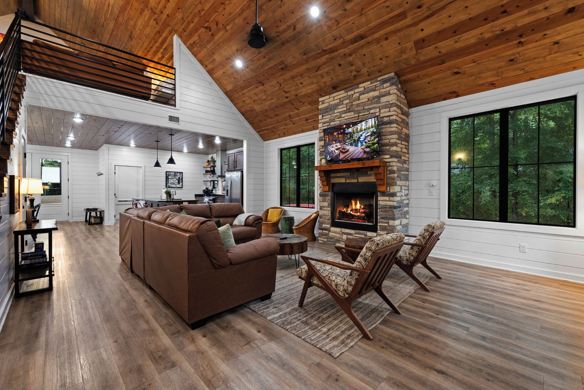 A spacious living room with a fireplace, wooden flooring, and large windows.