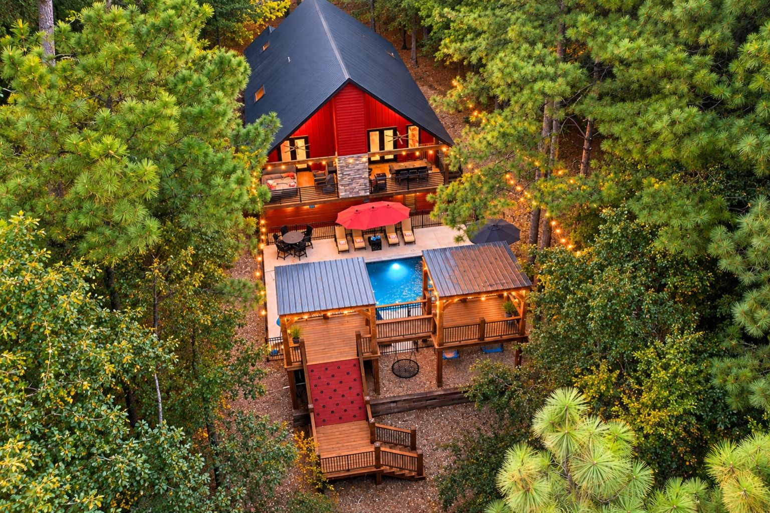 A cabin with a pool, deck, and outdoor seating area surrounded by trees.