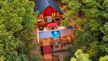 A cabin with a pool, deck, and outdoor seating area surrounded by trees.