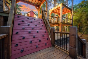 Eine Holzterrasse mit einer Kletterwand und einer Holztreppe, die zu einer erhöhten Ebene führt.