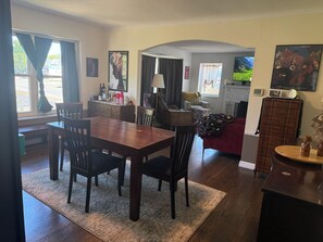 Ein Essbereich mit Holztisch und -stühlen, eine Küche im Hintergrund und ein Wohnzimmer mit einem roten Sofa.