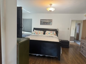 Ein Schlafzimmer mit einem Bett, einem Schreibtisch, einem Fernseher und einem Bild an der Wand.