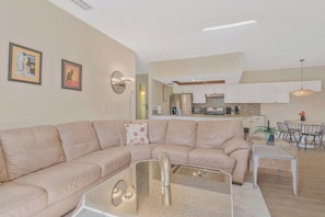A modern living room with a beige sectional sofa, a glass coffee table, and a dining area with a white table and chairs. - Spacious 2br-2ba townhome located in Saddlebrook (Zephyrhills)