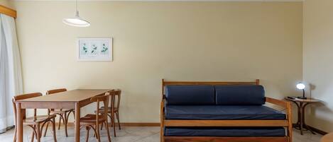 A room with a bed, a dining table with chairs, a framed picture on the wall, and a ceiling light.