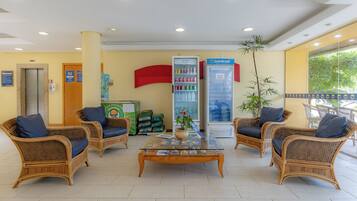 A reception area with wicker furniture, a glass coffee table, a refrigerator, and a plant.