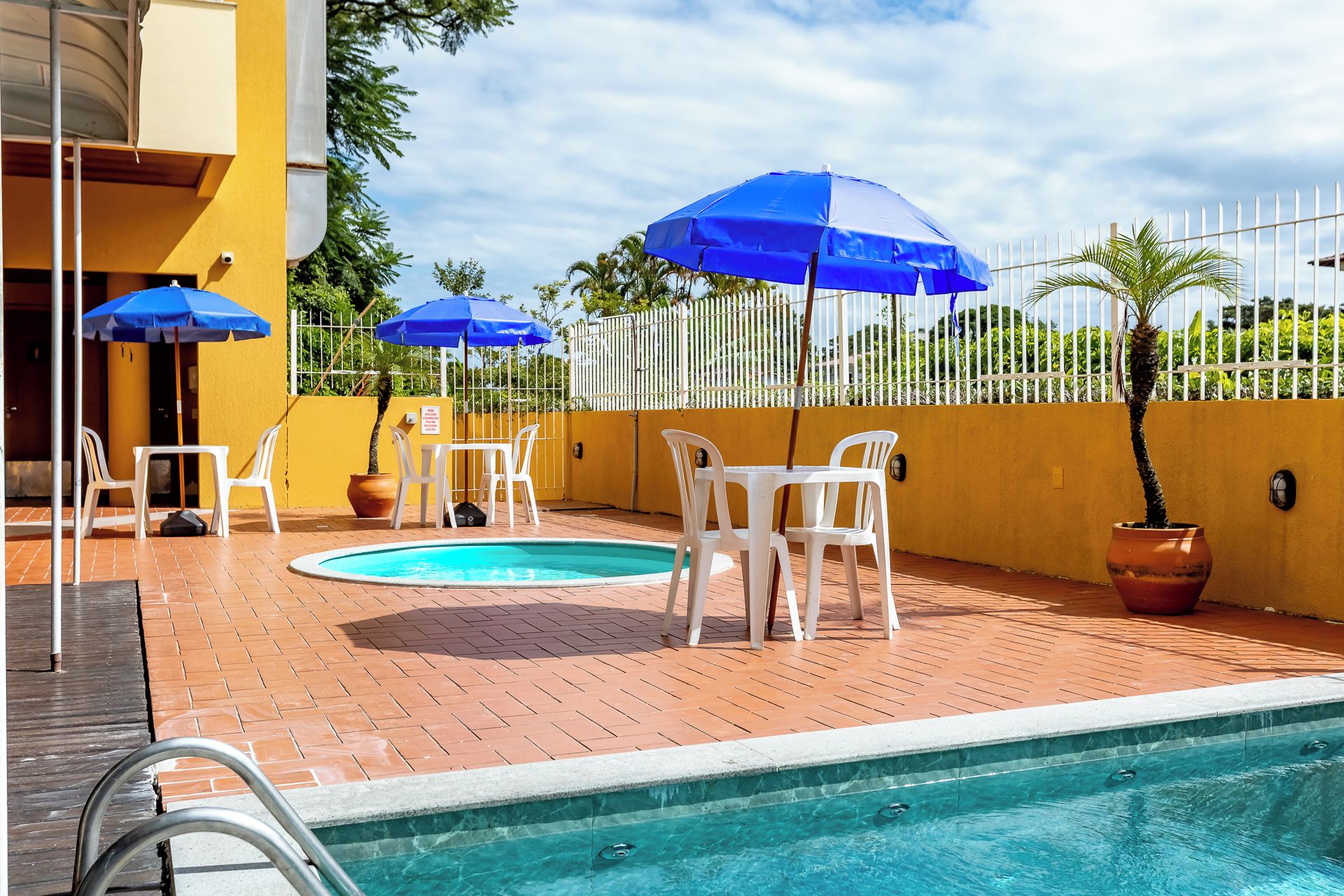 Ein Poolbereich mit zwei runden Pools, weißen Kunststoffstühlen und blauen Sonnenschirmen.