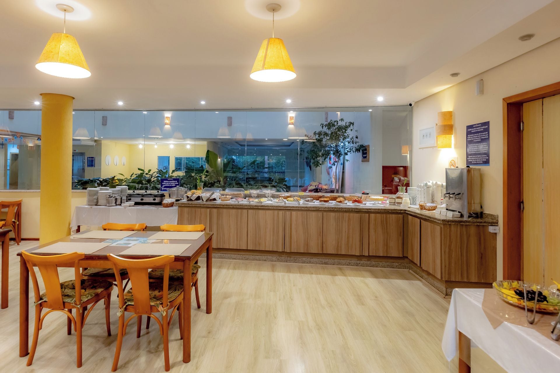A breakfast buffet area with a variety of food items, a seating area with tables and chairs, and a large window providing a view of the outdoors.