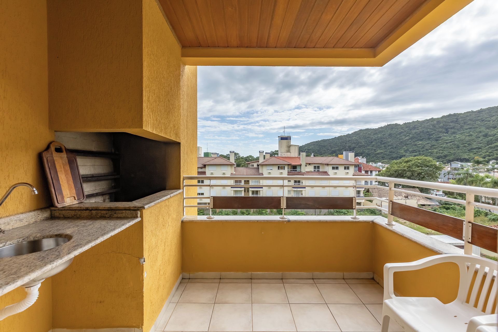 Un balcón con un lavamanos, una tabla de cortar de madera y vistas a una zona residencial con edificios y colinas.