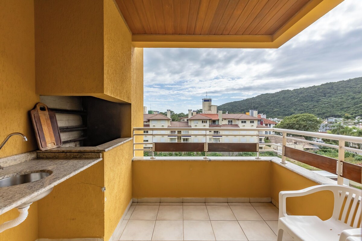 Un balcón con un lavamanos, una tabla de cortar de madera y vistas a una zona residencial con edificios y colinas.