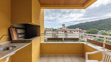 Un balcón con un lavamanos, una tabla de cortar de madera y vistas a una zona residencial con edificios y colinas.