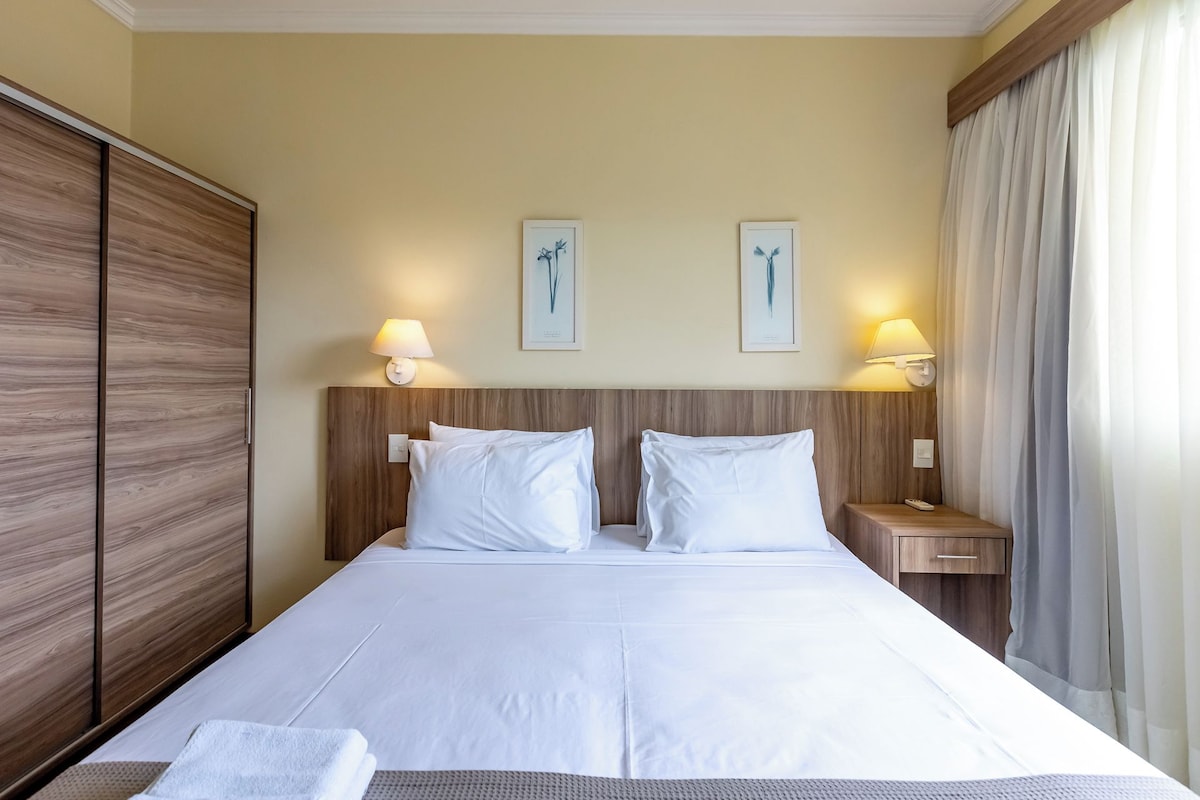 Habitación de hotel con una cama grande, dos lámparas fijadas a la pared y una mesita de noche con un control remoto.