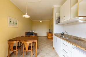 A compact kitchen with white cabinets, a granite countertop, and a dining area with wooden chairs.