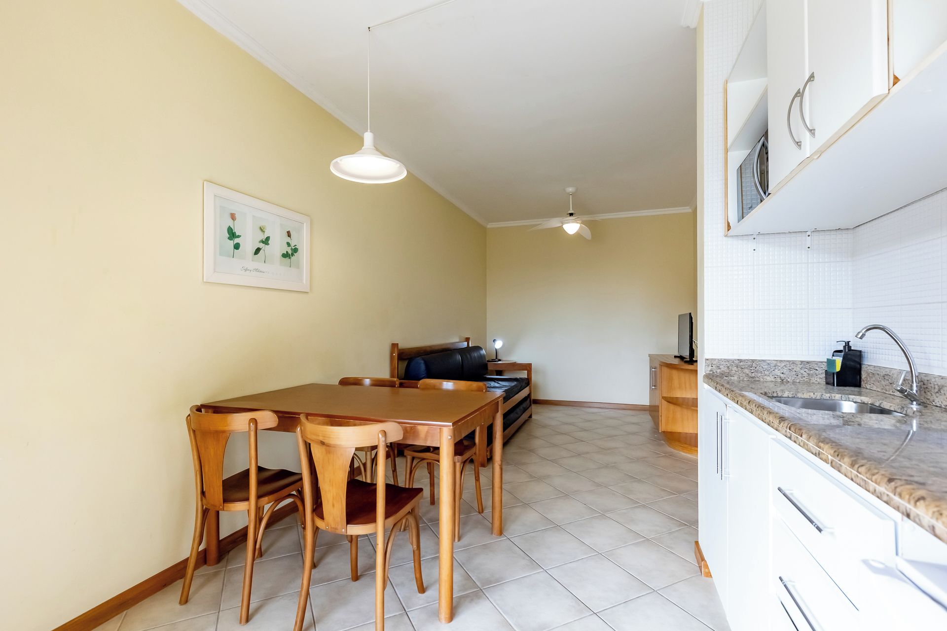Een eethoek met een houten tafel en stoelen, een plafondventilator, en een keuken met een spoelbak en kastjes.