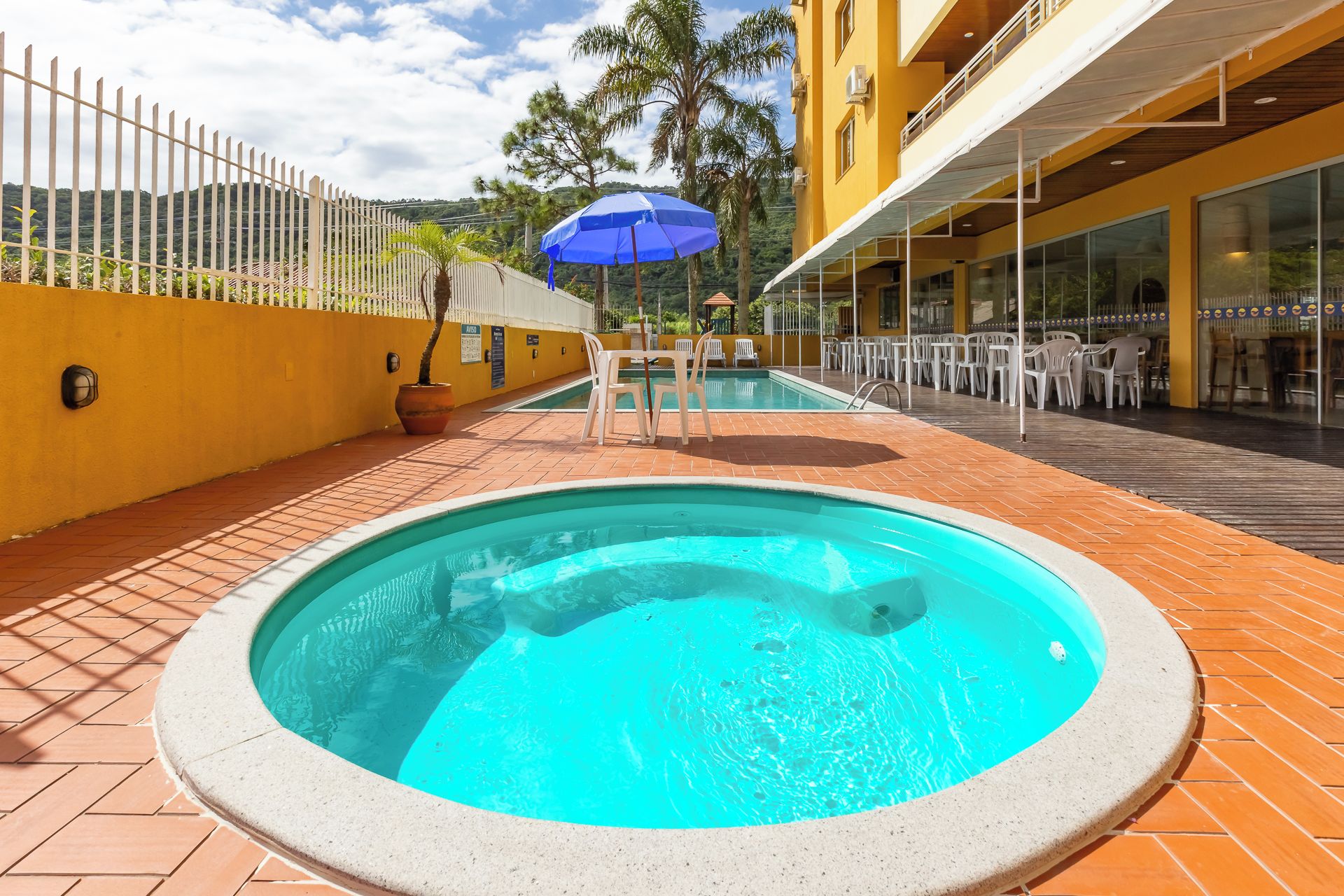 Una piscina con un jacuzzi integrado, rodeada por una terraza con mobiliario exterior y un edificio de fachada amarilla.