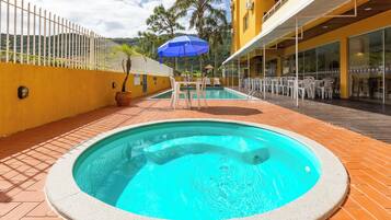 Una piscina con un jacuzzi integrado, rodeada por una terraza con mobiliario exterior y un edificio de fachada amarilla.