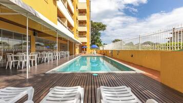 A pool area with lounge chairs, a pool, and a building with balconies.