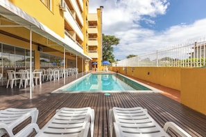 A pool area with lounge chairs, a pool, and a building with balconies. - Parador da Cachoeira By Candeias (Florianópolis)
