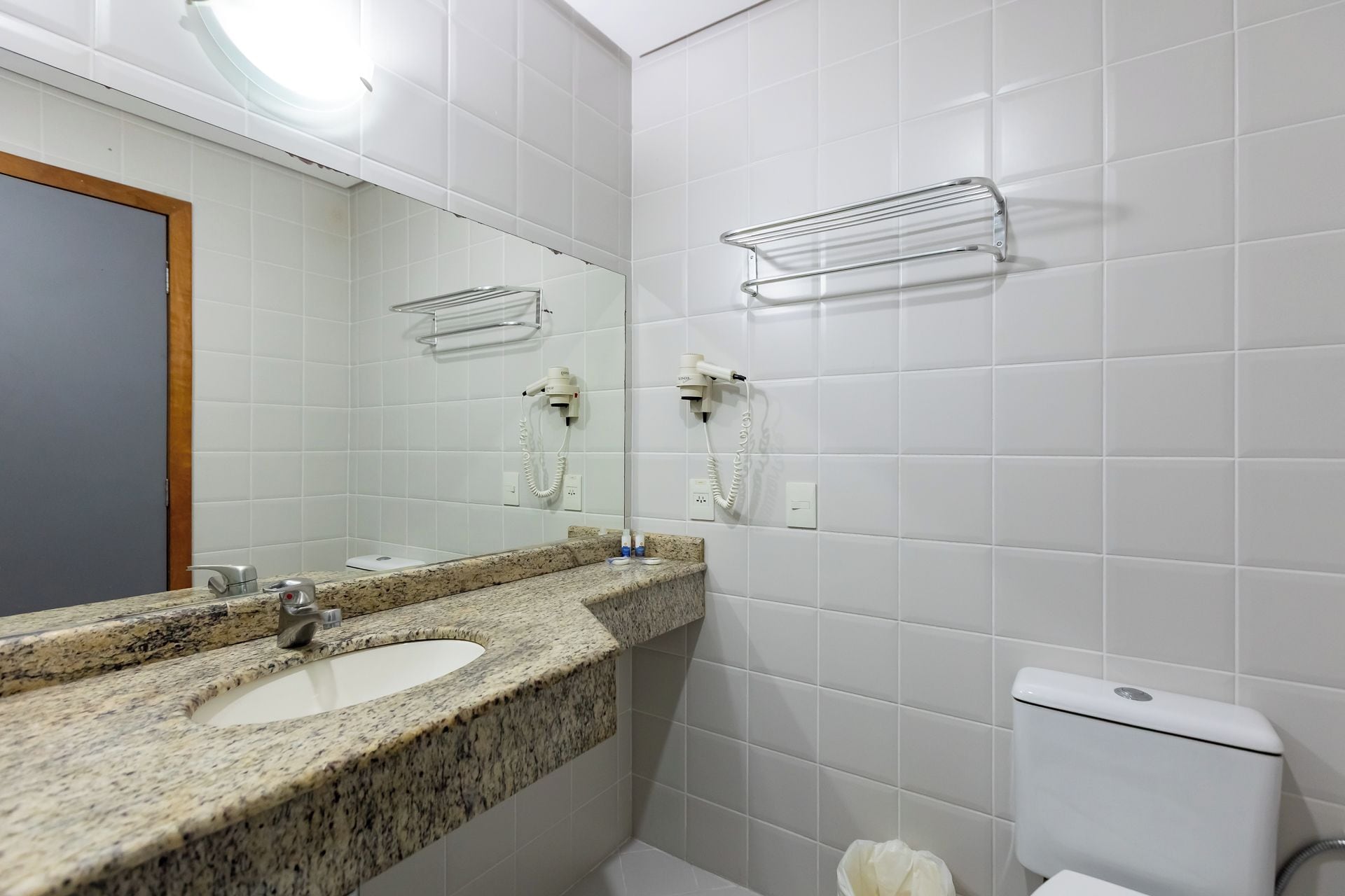 Un baño con lavamanos de encimera de granito, un espejo, toallero y un inodoro.