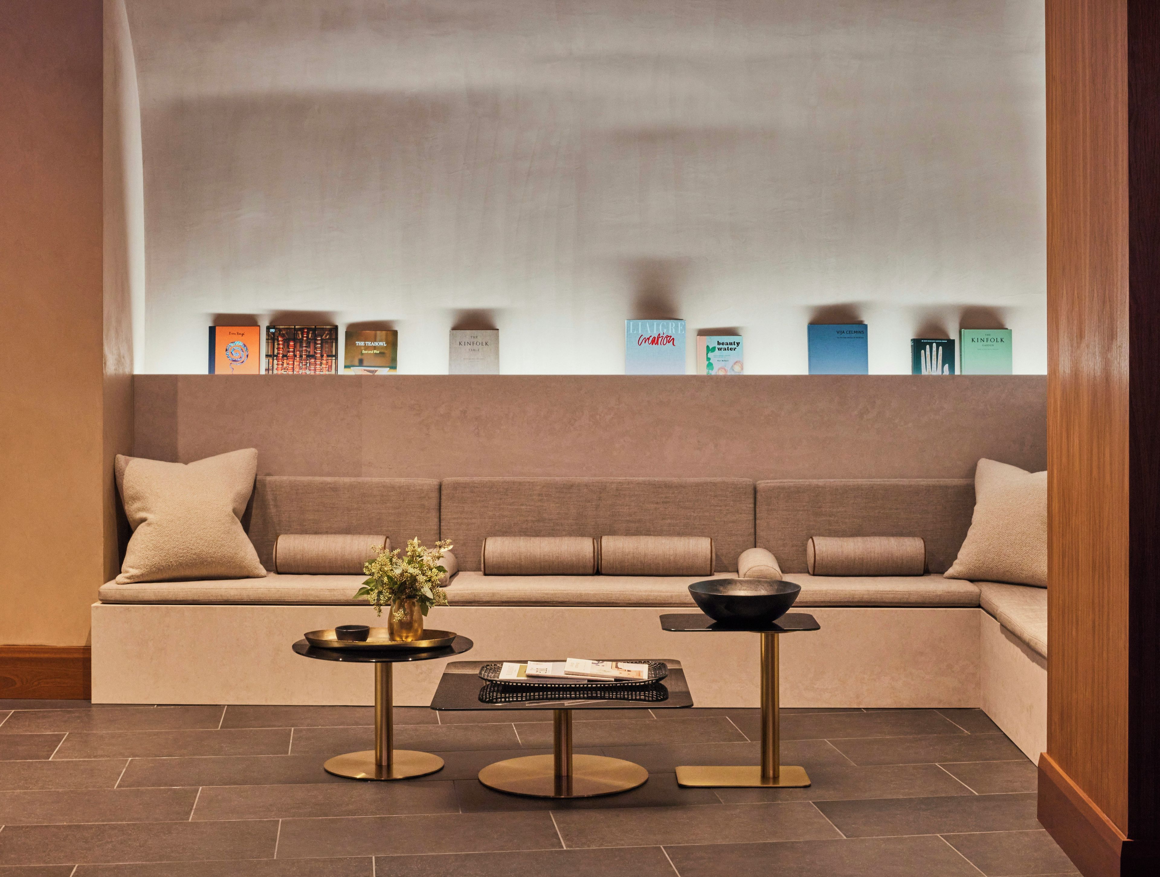 Una sala de estar moderna con un sofá, dos mesas de centro y una estantería llena de libros y objetos decorativos.