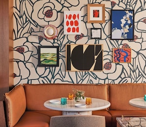 A room with a patterned wallpaper, a brown sofa, a round table with a vase and candles, and various framed artworks on the wall. - Omni Boston Hotel at the Seaport Artist Tower Experience (Boston)
