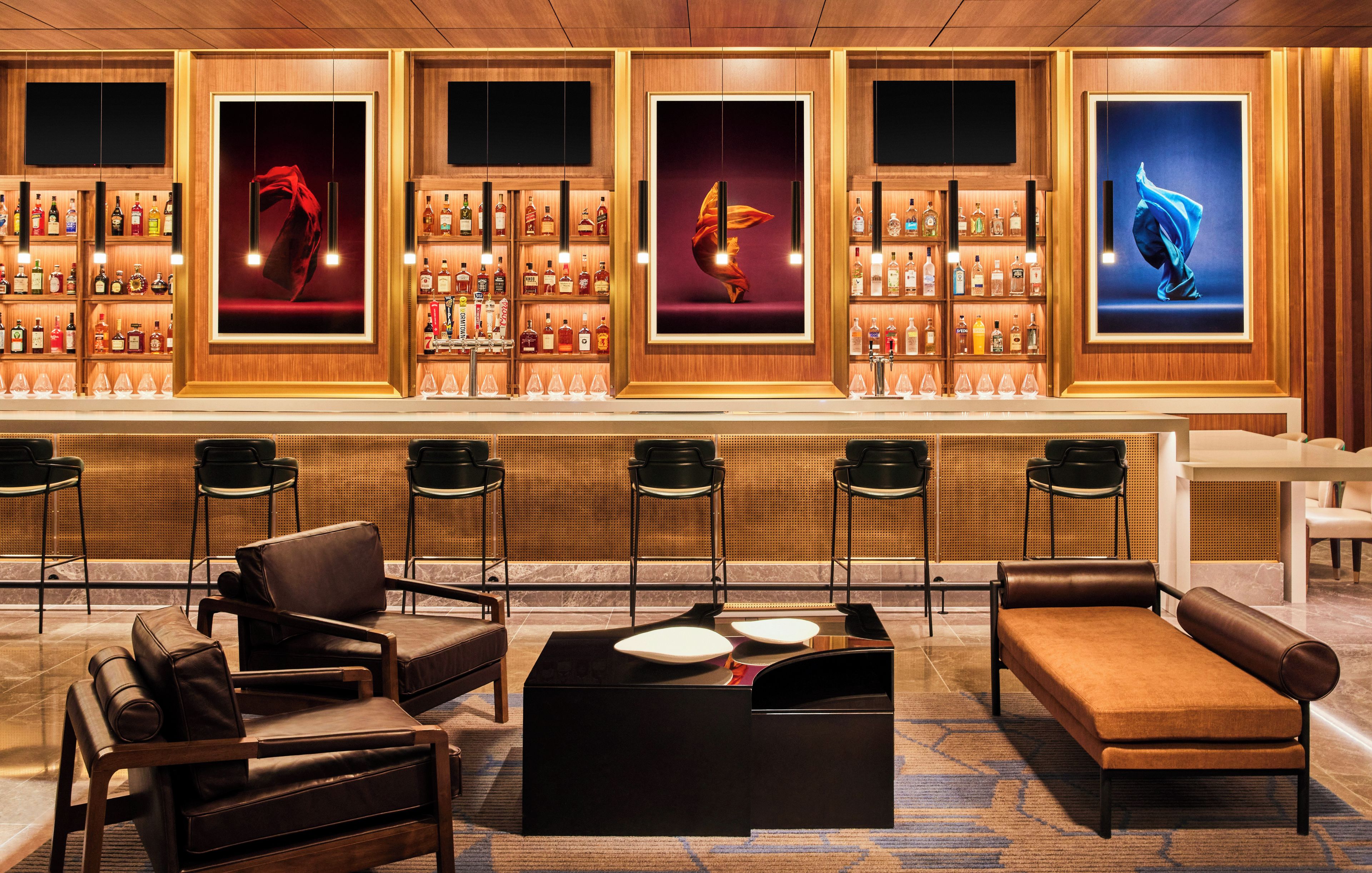 A bar area with multiple shelves of liquor bottles, bar stools, and a seating area with a sofa and chairs.