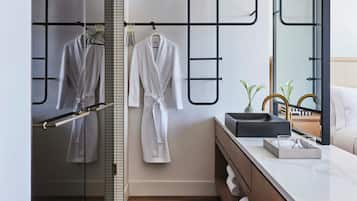 Uma casa de banho moderna com cabine de duche em vidro, um roupeiro branco pendurado num suporte de metal preto e uma toucador com bancada de mármore.