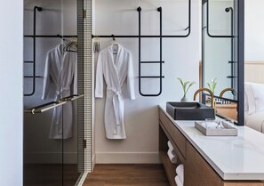 Une salle de bain moderne avec une douche à parois de verre, un peignoir blanc suspendu à un porte-serviettes en métal noir et un meuble-lavabo doté d’un plan de travail en marbre.