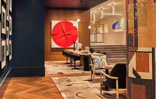Un interior moderno con una gran obra de arte circular roja, suelo de madera y mobiliario contemporáneo.