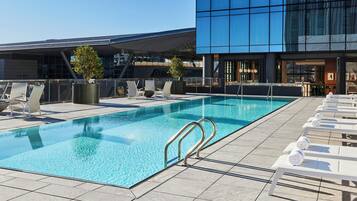 Una piscina en la azotea con sillones de descanso y un edificio moderno al fondo.