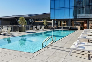 Une piscine sur le toit, avec des chaises longues, et un bâtiment moderne en arrière-plan.