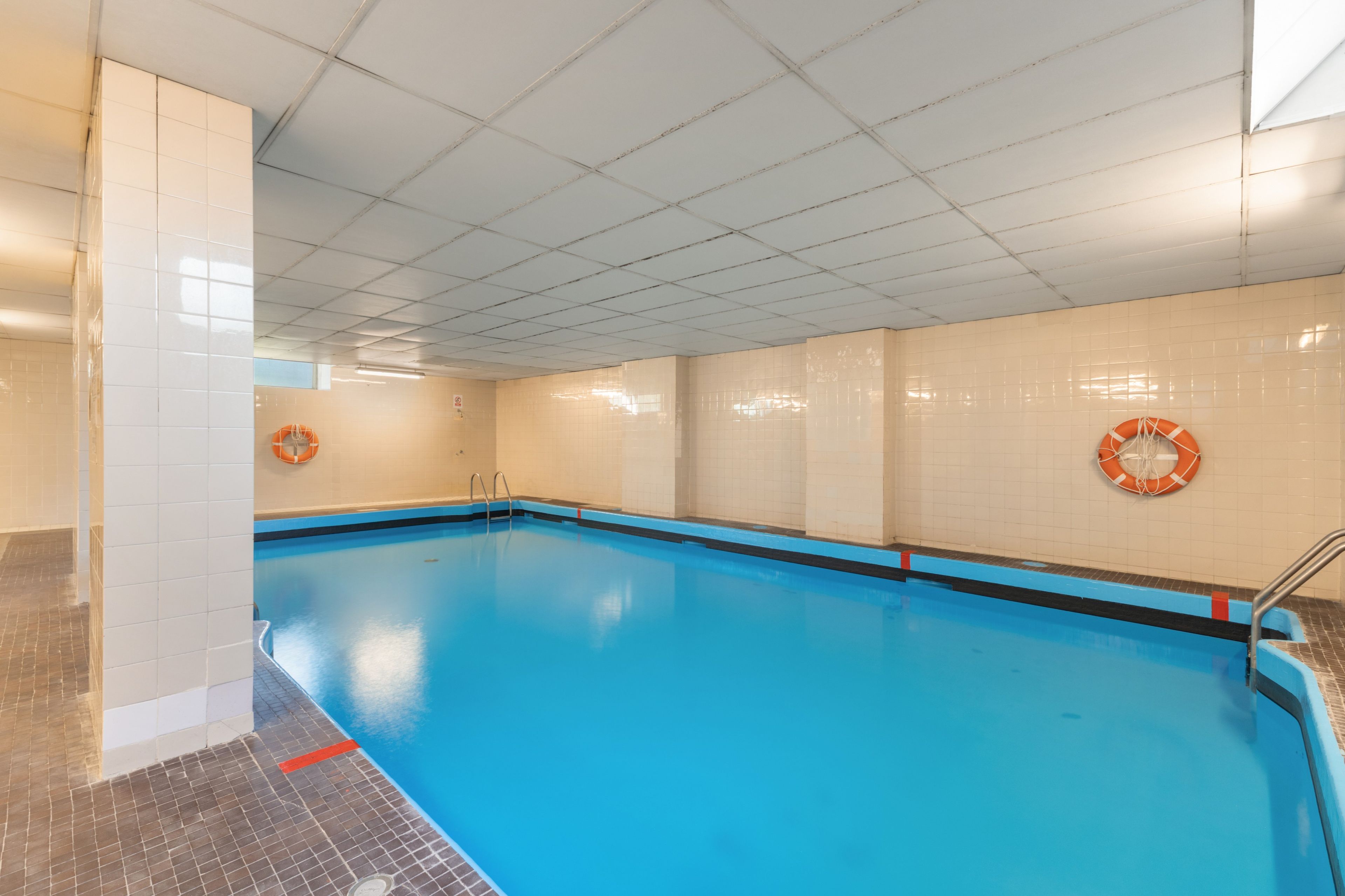 Una piscina interior con agua cristalina, paredes y piso de cerámica.