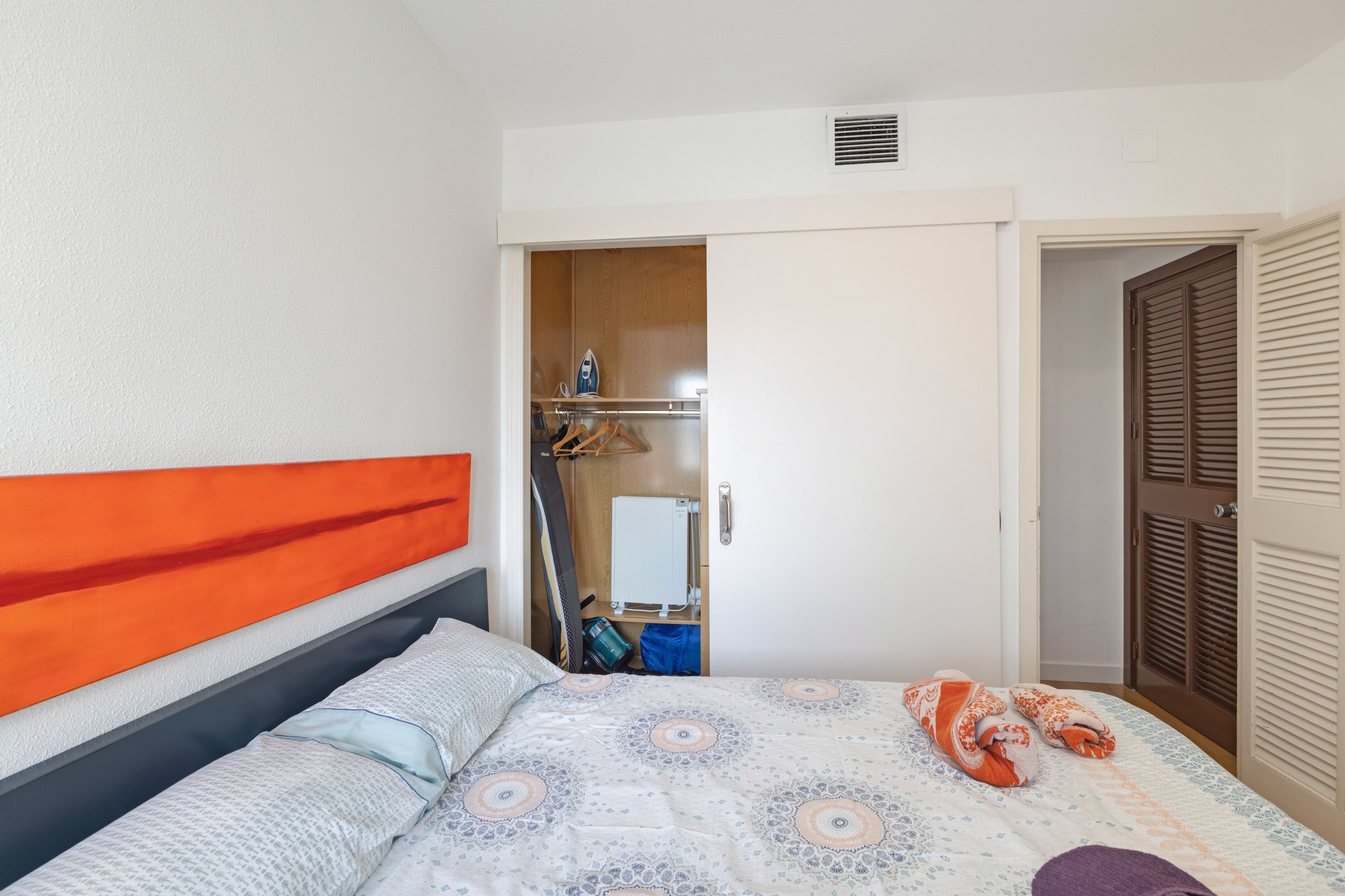 Un dormitorio con cama, armario y baño visible a través de una puerta abierta.