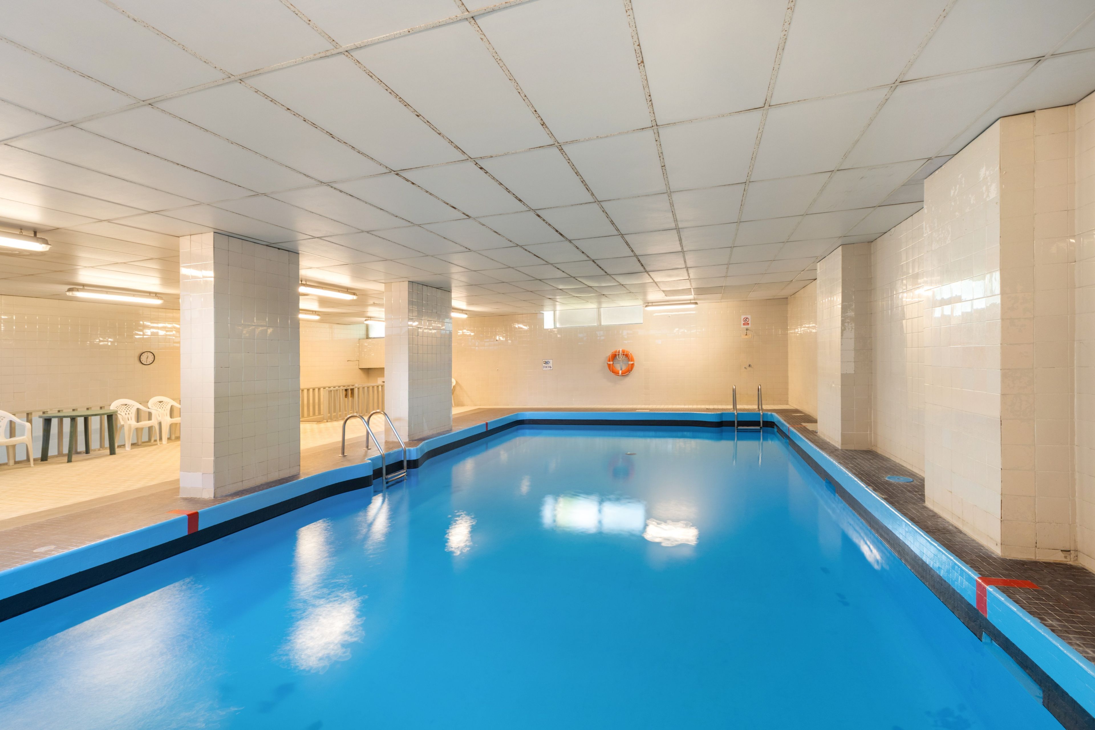 Una piscina interior con agua azul cristalina, paredes con azulejos y un flotador en la pared.