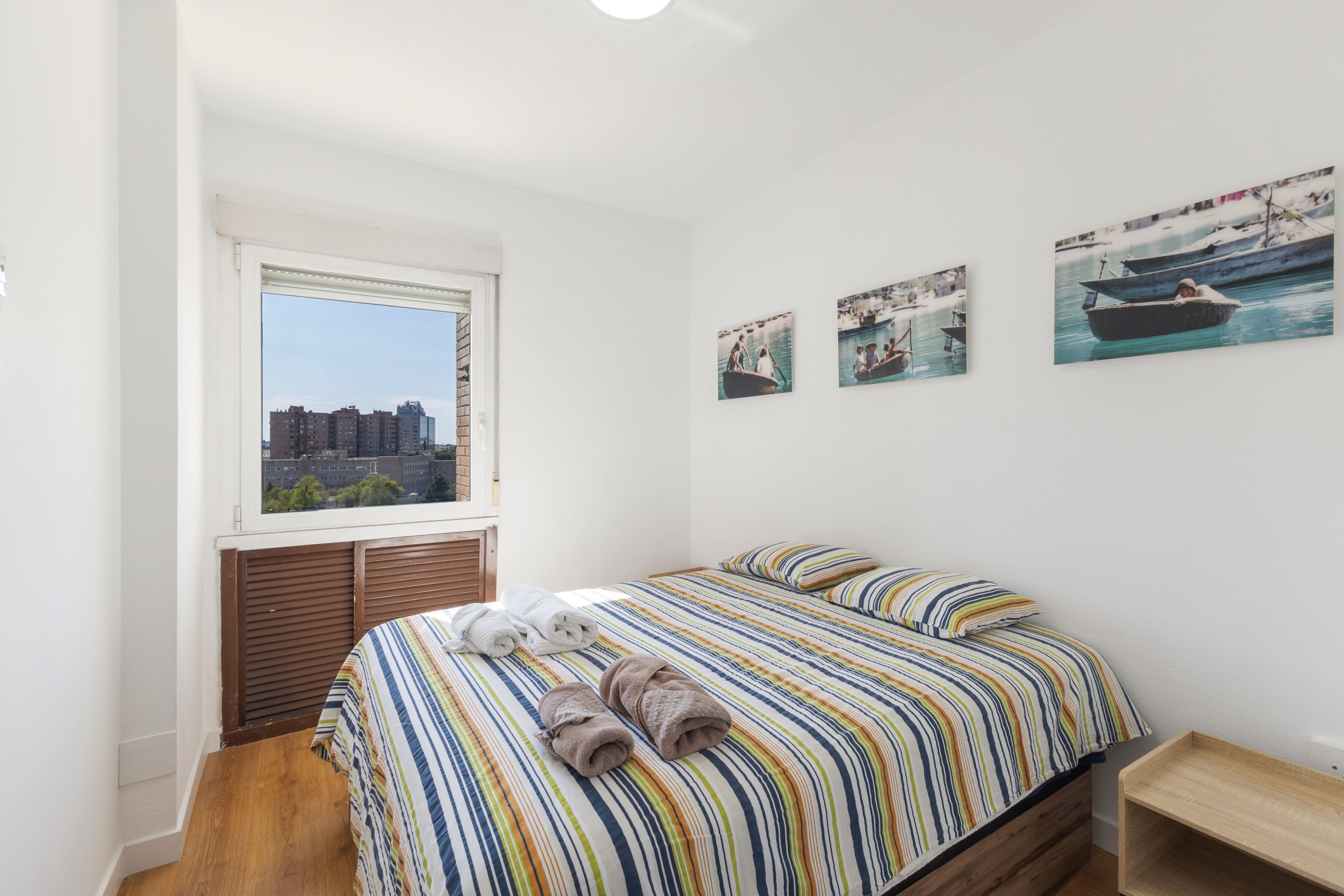 Een slaapkamer met een bed, een raam en drie ingelijste foto’s aan de muur.