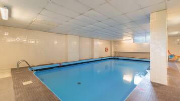 Una piscina interior con suelo y paredes de azulejos, un flotador en la pared y una escalera metálica que da acceso a la piscina.