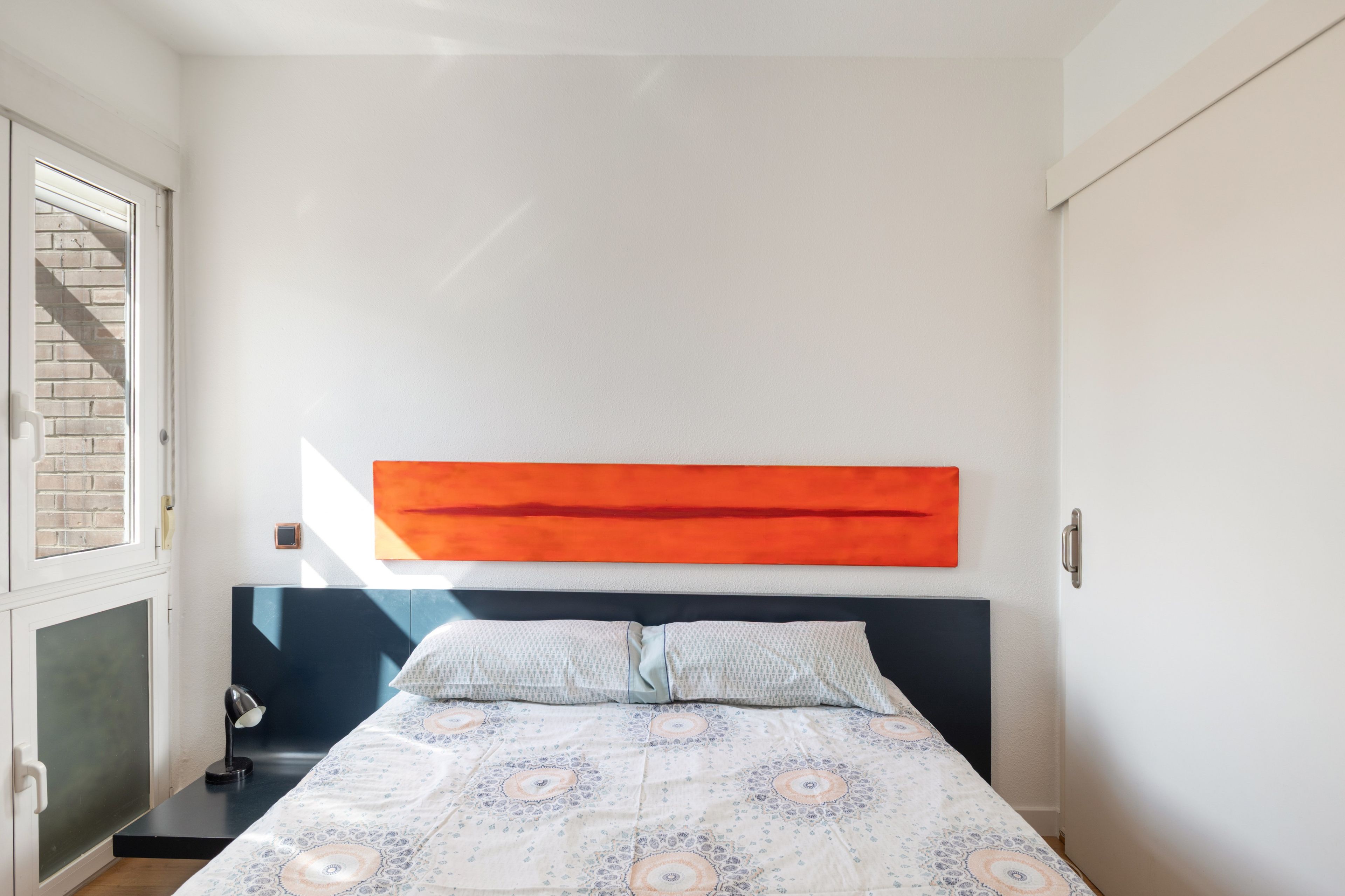 Un dormitorio con cama, ventana, puerta y una obra de arte colgada en la pared.