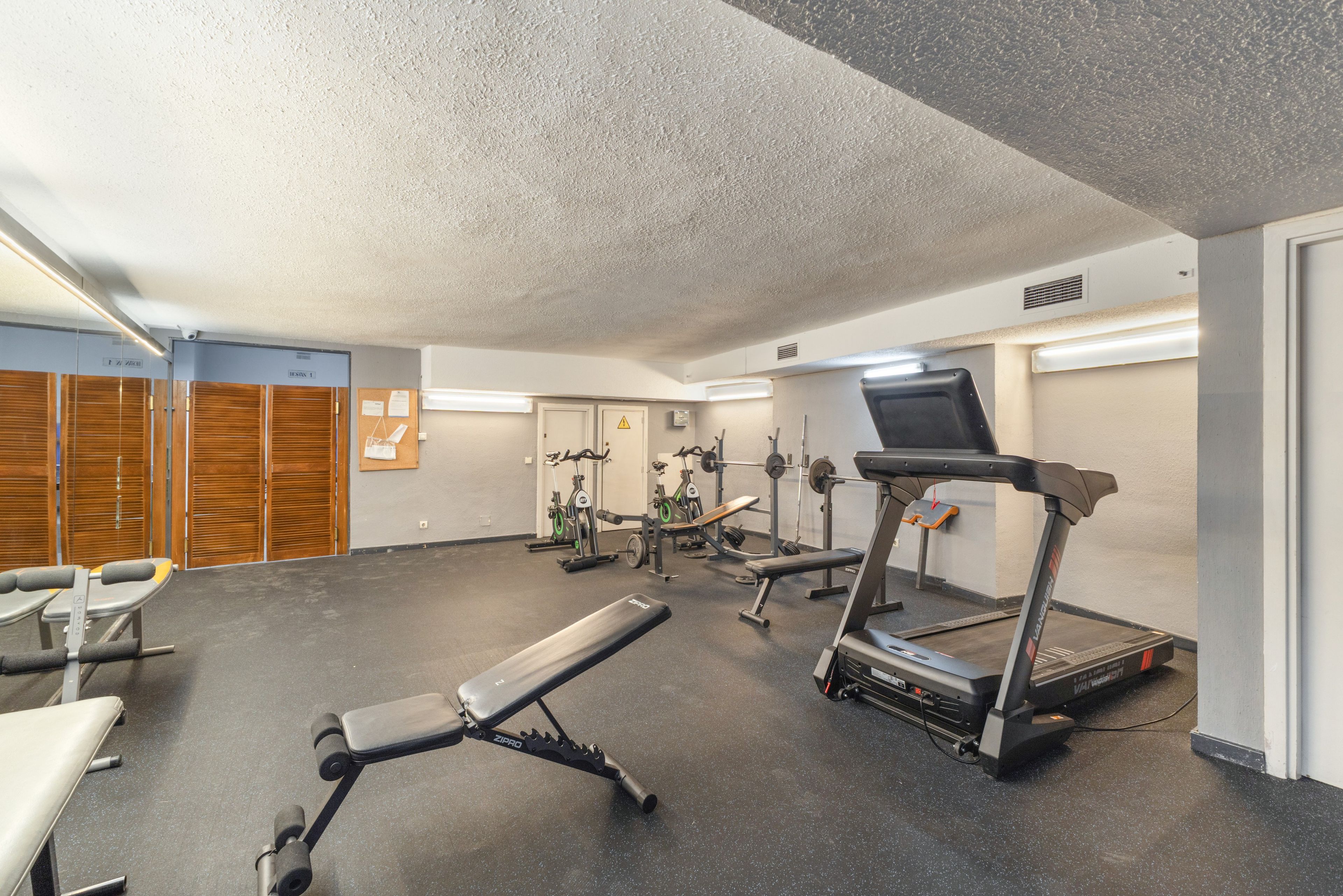 Un gimnasio con equipamiento de ejercicio, incluyendo una cinta de correr, banca de pesas y bicicletas estáticas.